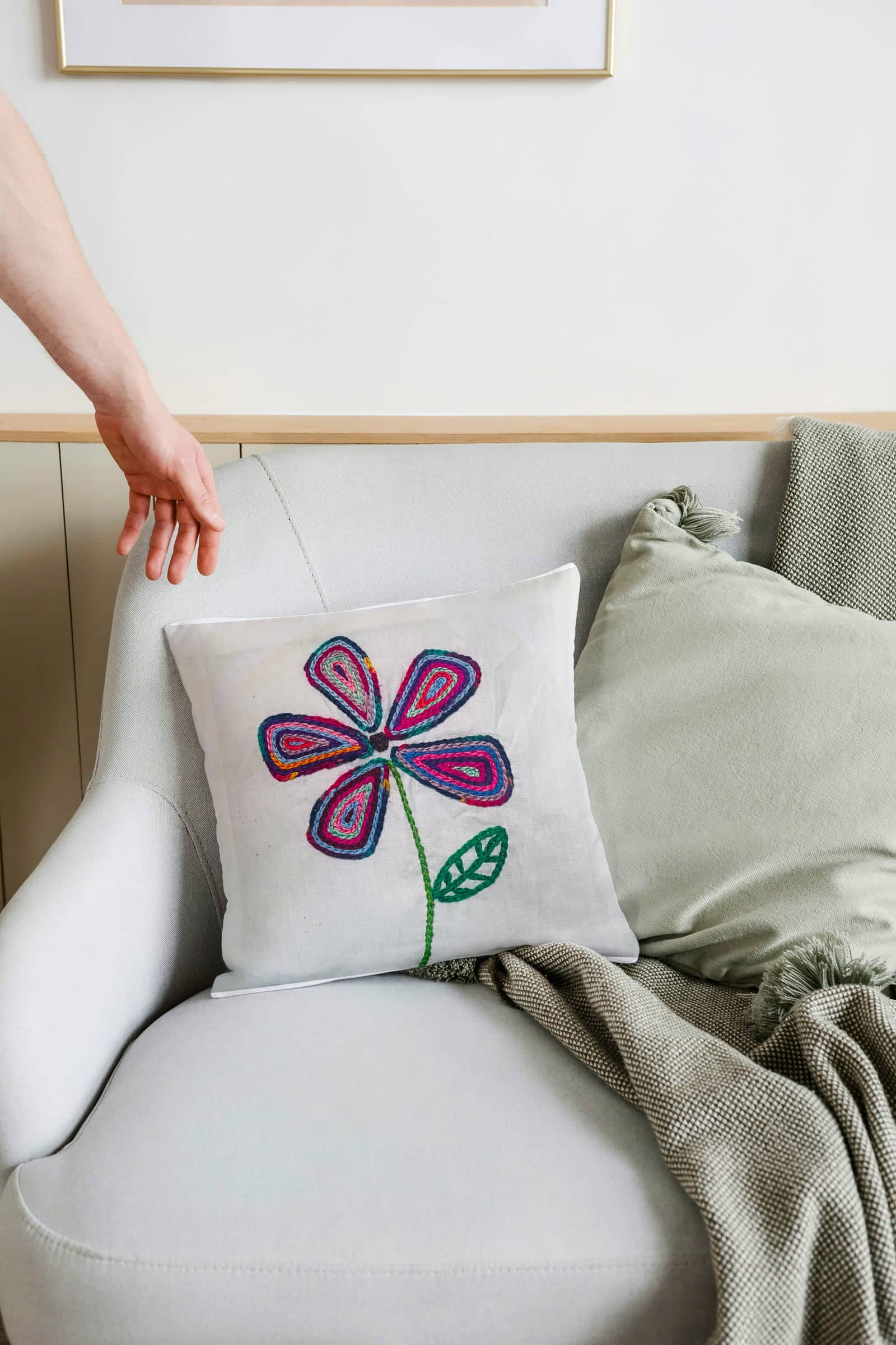 Hand holding a cushion embroidered with a pink and purple flower